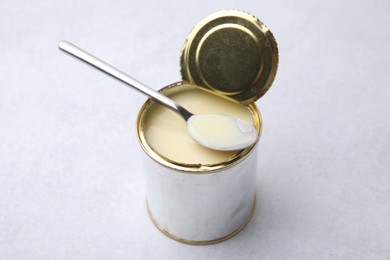 Photo of Open tin can with condensed milk and spoon on white table