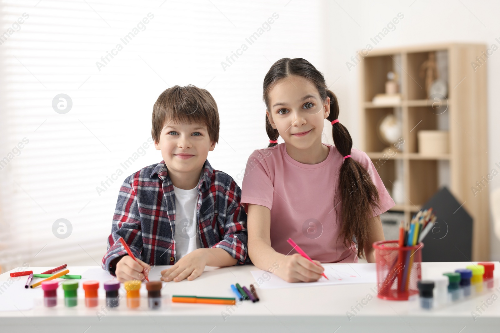 Photo of Happy brother and sister drawing at white table in room