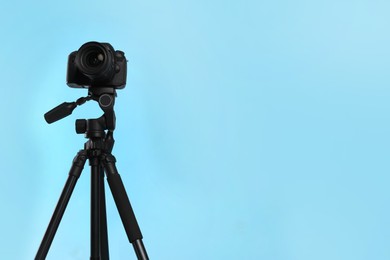 Photo of Modern tripod with professional camera on light blue background. Space for text