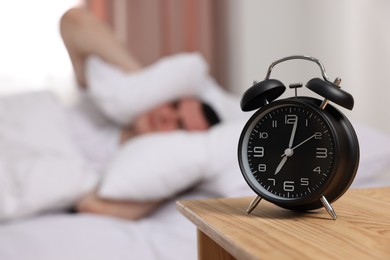 Man covering his ears with pillows in bedroom, focus on alarm clock. Space for text