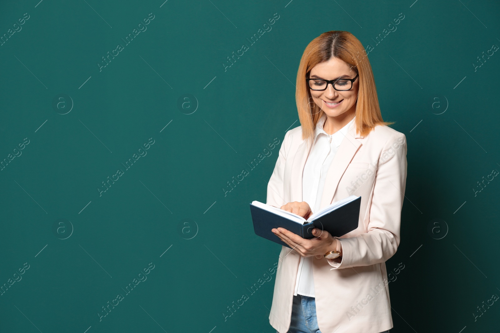 Photo of Portrait of beautiful teacher with book near chalkboard, space for text