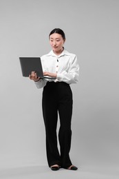 Photo of Full length portrait of businesswoman with laptop on grey background