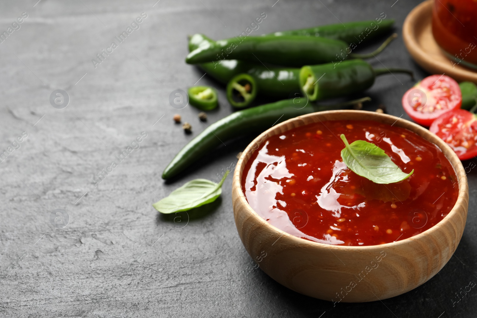 Photo of Spicy chili sauce with basil in bowl on black table, space for text