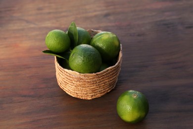 Photo of Fresh ripe limes in wicker basket on wooden table