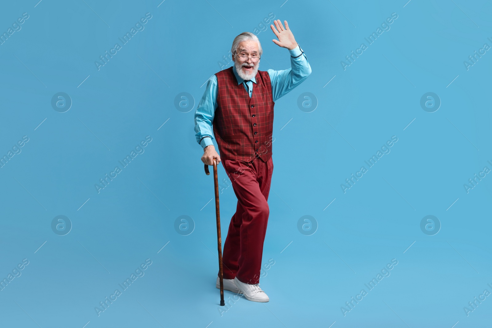 Photo of Senior man with walking cane waving on light blue background