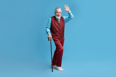 Photo of Senior man with walking cane waving on light blue background