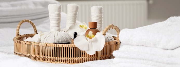 Image of Wicker tray with herbal bags and other spa products on white bath towel. Banner design