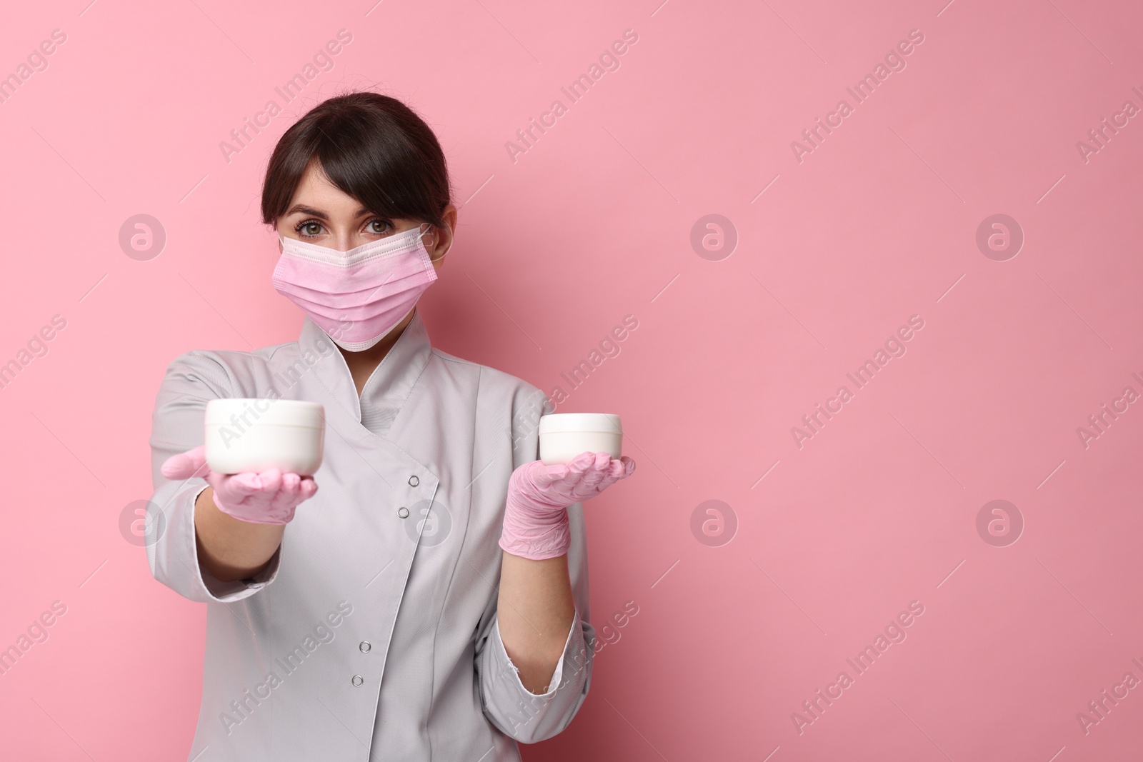 Photo of Cosmetologist with cosmetic products on pink background, space for text