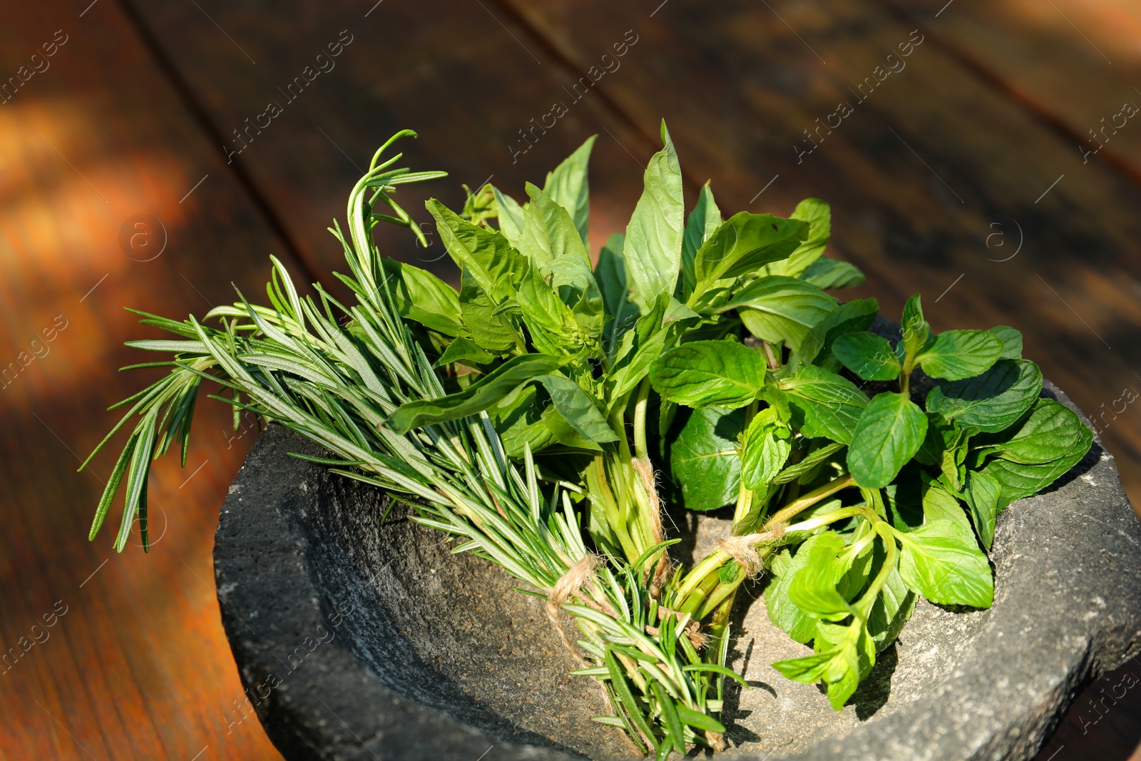 Photo of Mortar with thyme, rosemary and basil on wooden table, closeup. Aromatic herbs