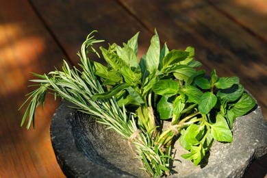 Mortar with thyme, rosemary and basil on wooden table, closeup. Aromatic herbs