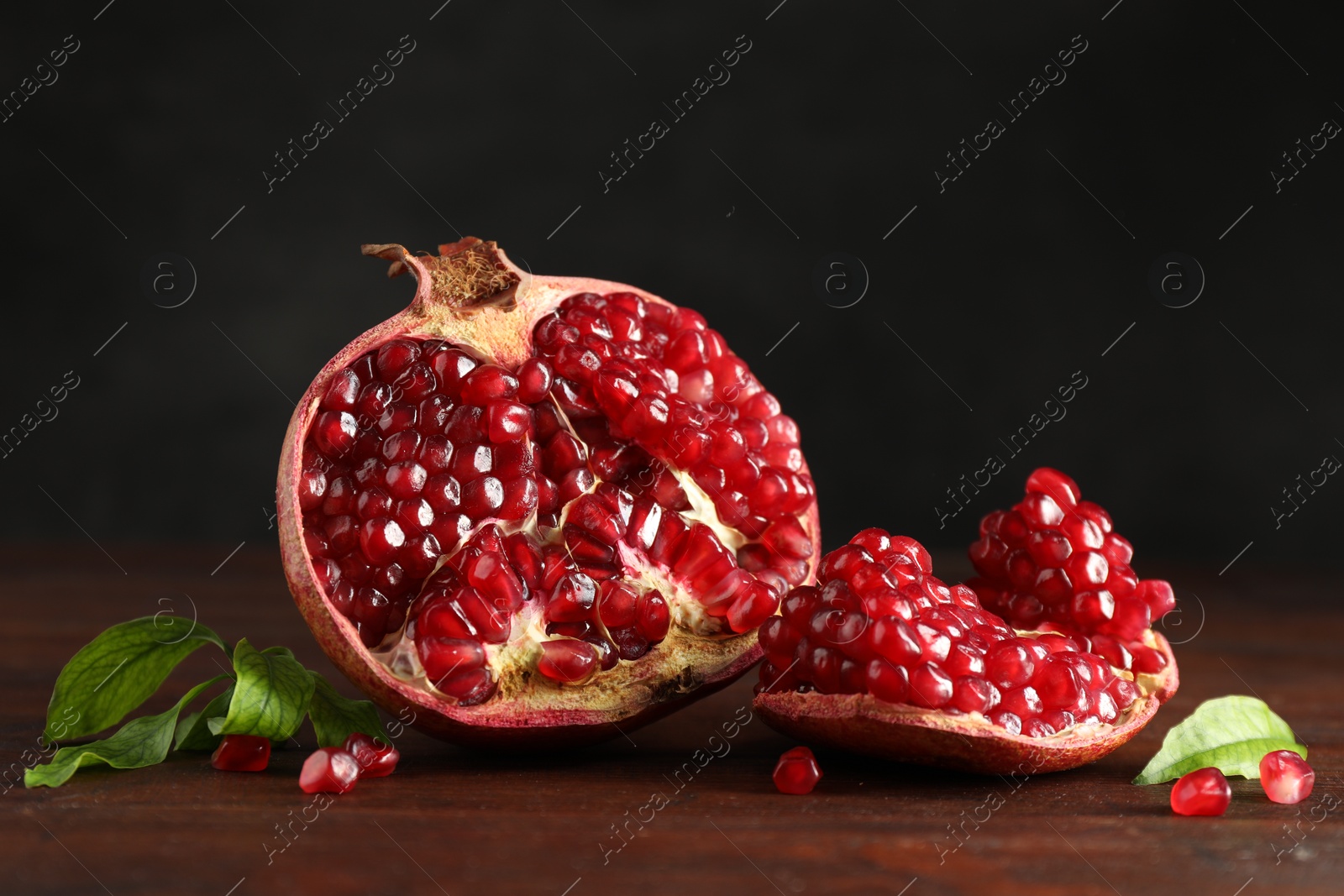 Photo of Cut fresh pomegranate and green leaves on wooden table