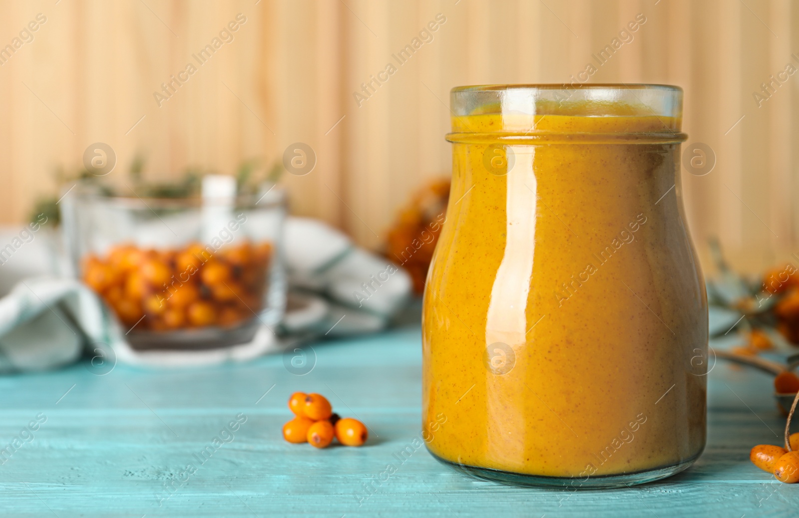 Photo of Delicious sea buckthorn jam and fresh berries on light blue wooden table. Space for text