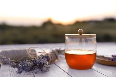 Jar with fresh honey and lavender flowers on white wooden table outdoors. Space for text