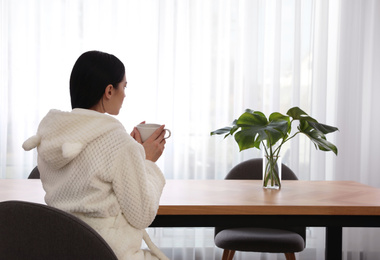 Woman at table with fresh leaves of tropical plants in room. Home design ideas