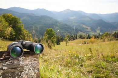Photo of Modern binoculars on wooden log in mountains, space for text