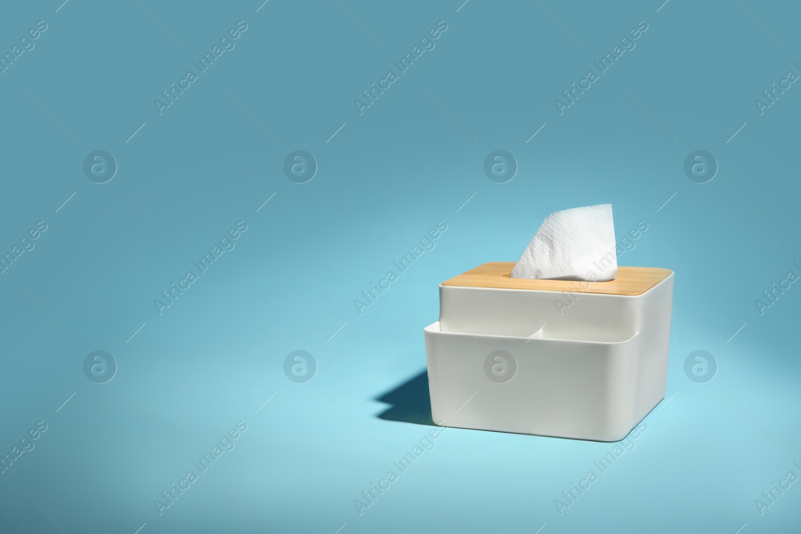 Photo of Holder with paper tissues on light blue background. Space for text