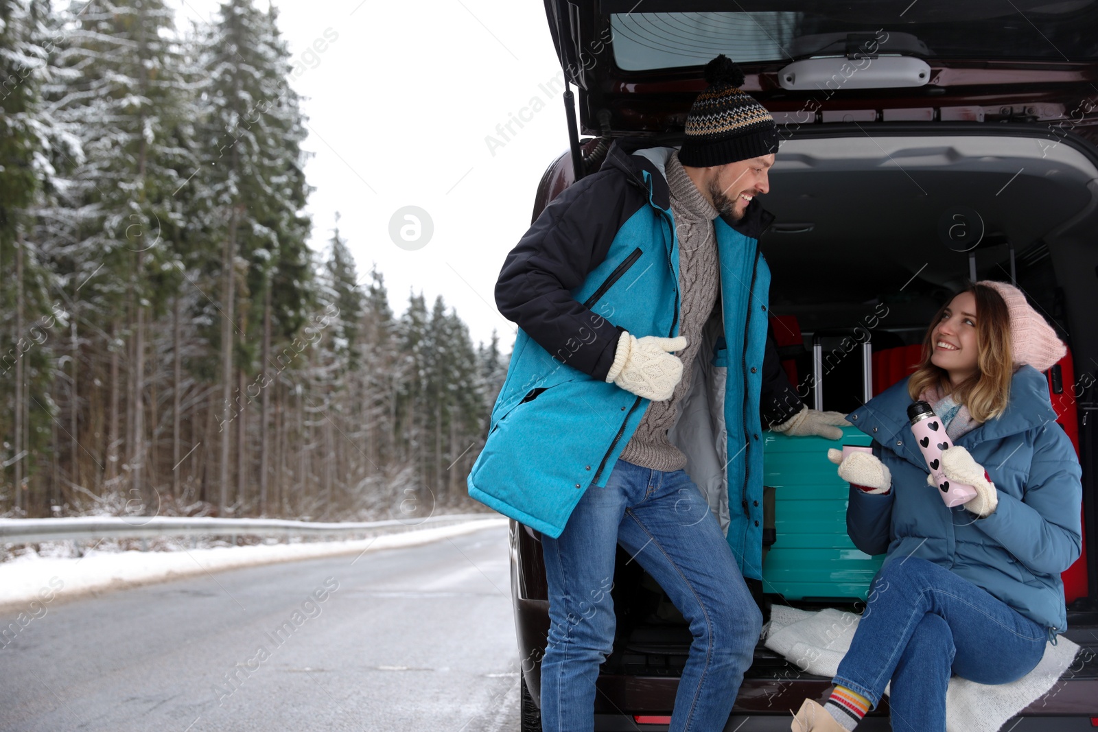 Photo of Couple near open car trunk full of luggage on road, space for text. Winter vacation