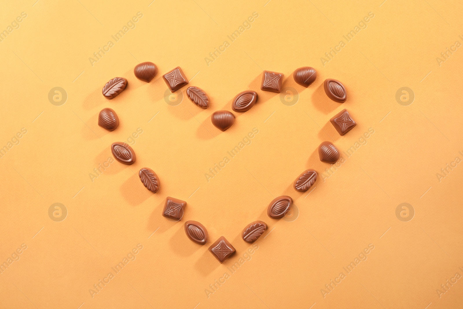 Photo of Heart made with delicious chocolate candies on brown background, top view