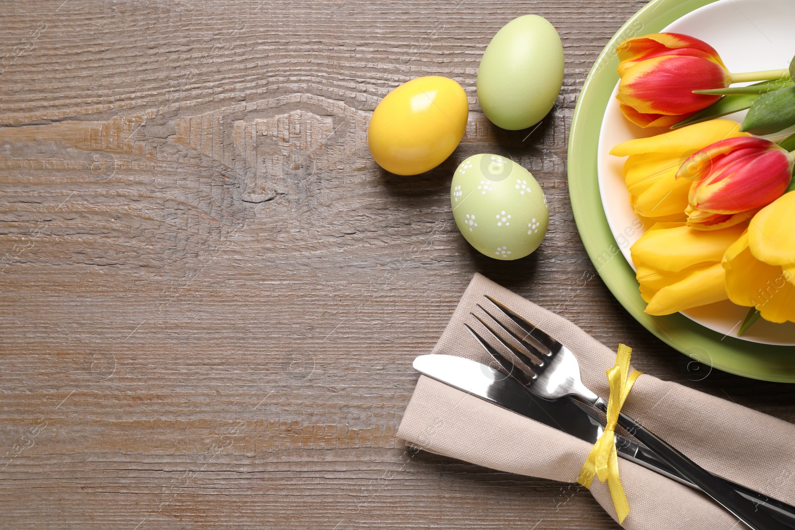 Photo of Festive Easter table setting with painted eggs and flowers on wooden background, flat lay. Space for text