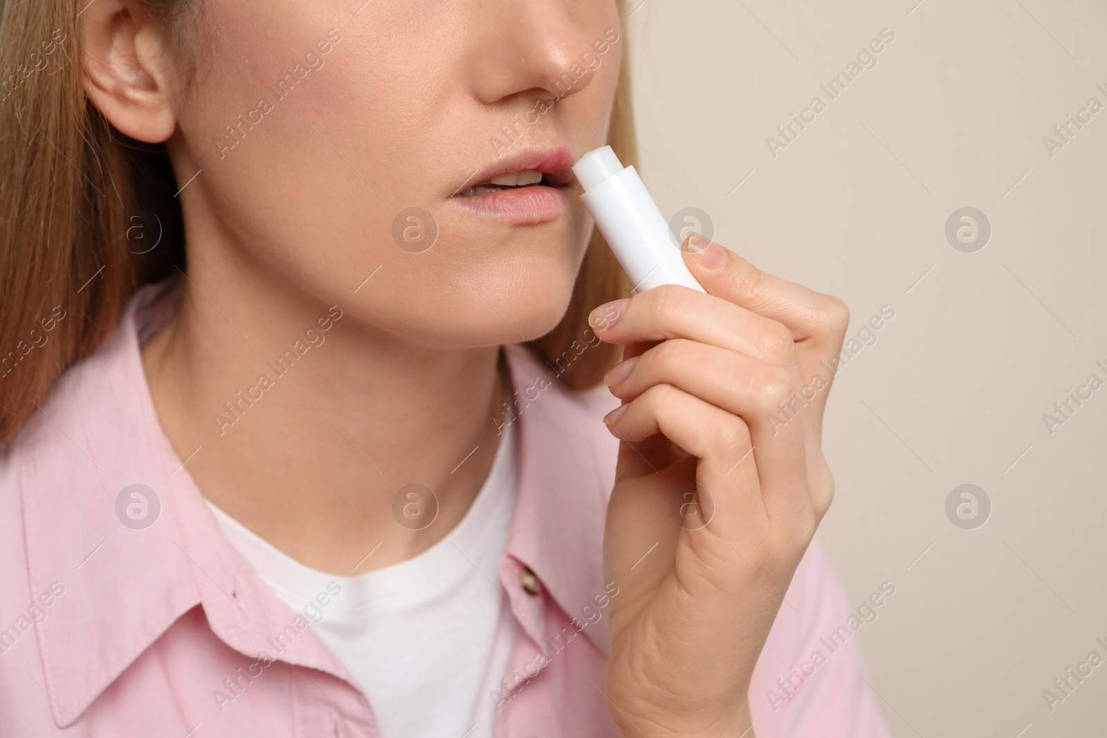 Photo of Woman with herpes applying lip balm against beige background, closeup