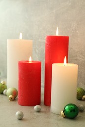 Photo of Burning candles with Christmas baubles on light grey table