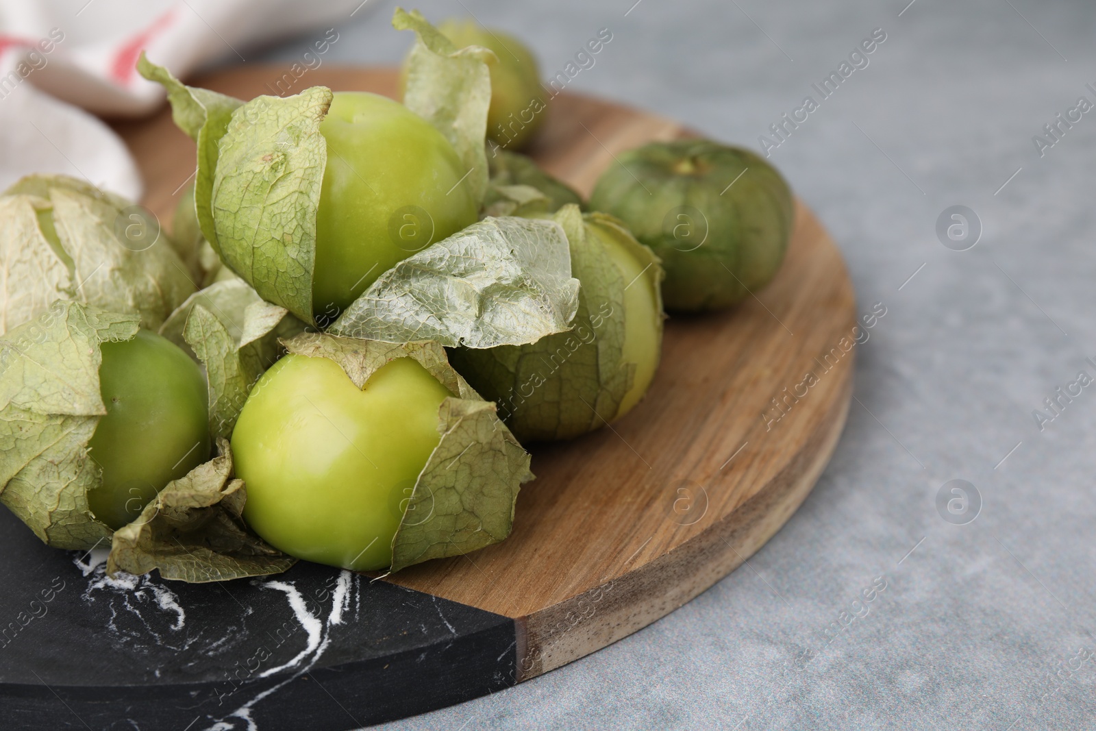 Photo of Fresh green tomatillos with husk on gray table, closeup