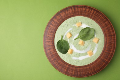 Photo of Delicious spinach cream soup with leaves and cheese in bowl on green background, top view. Space for text