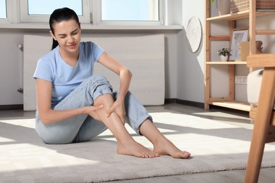 Photo of Young woman rubbing sore leg at home. Space for text