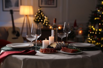 Photo of Christmas table setting with burning candles, appetizers and dishware in room