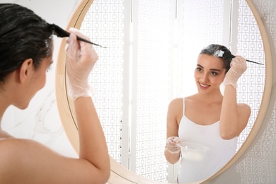 Photo of Young woman dyeing her hair in front of mirror at home