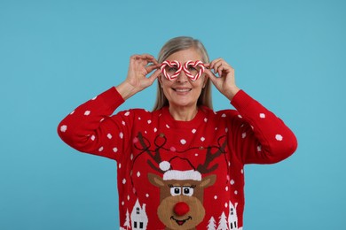 Photo of Senior woman in Christmas sweater and funny glasses on light blue background