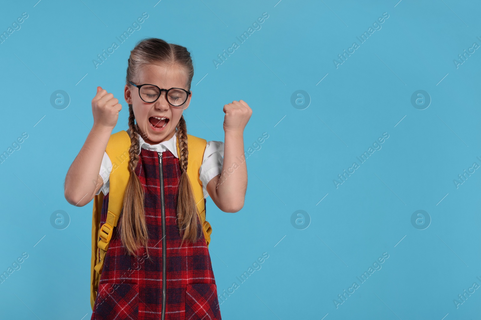 Photo of Emotional schoolgirl in glasses with backpack on light blue background, space for text