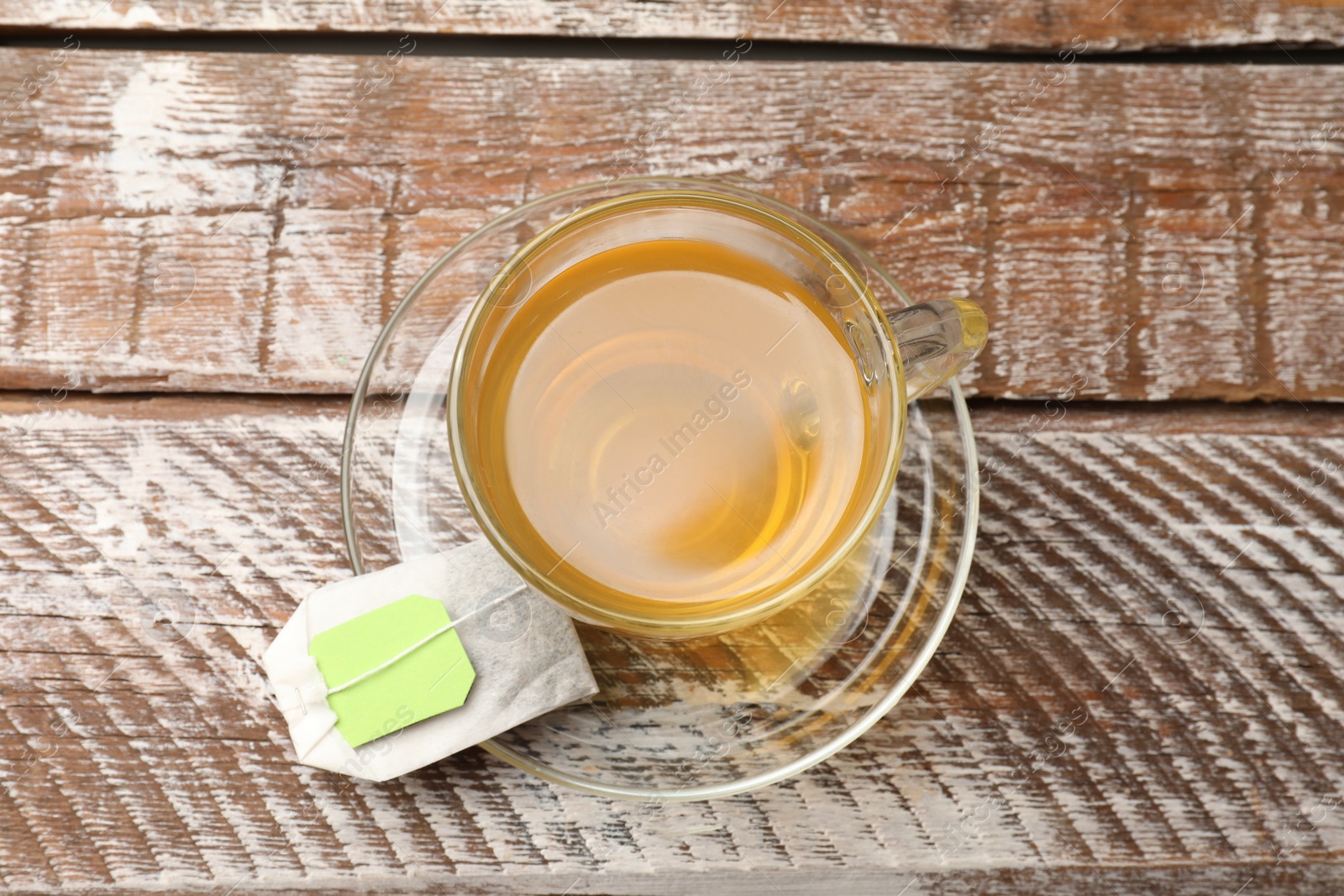 Photo of Tea bag in glass cup on wooden table, top view