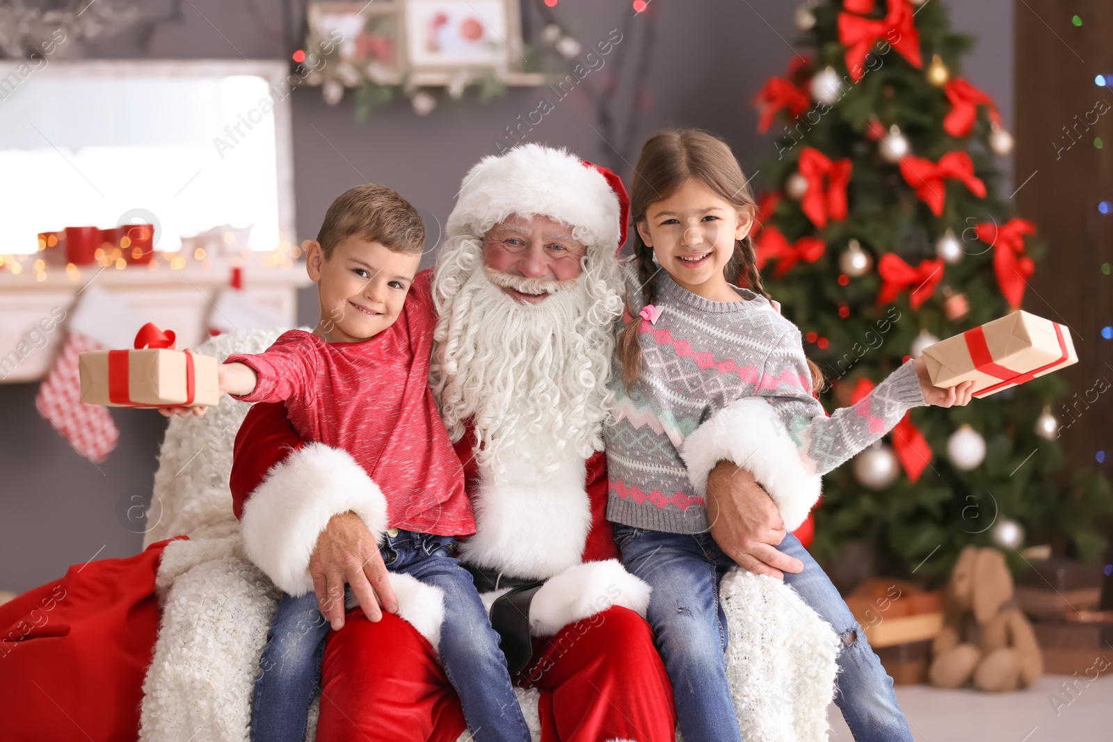 Photo of Little children with gift boxes sitting on authentic Santa Claus' knees indoors