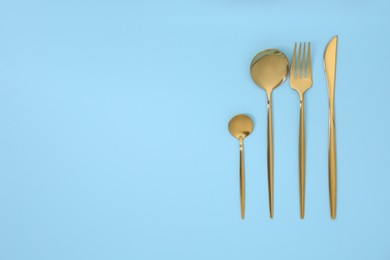 Photo of Stylish golden cutlery set on light blue background, flat lay. Space for text