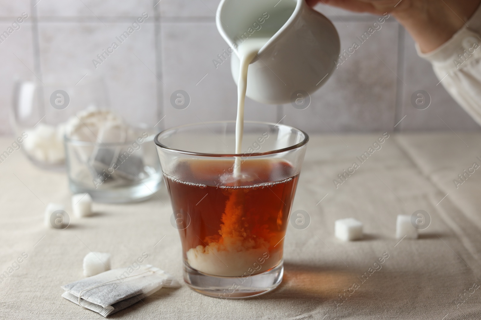 Photo of Pouring milk into cup with tea on light table, closeup