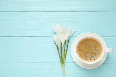 Photo of Cup of morning coffee and crocuses on light blue wooden table, flat lay. Space for text