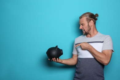 Emotional man with piggy bank on color background. Space for text