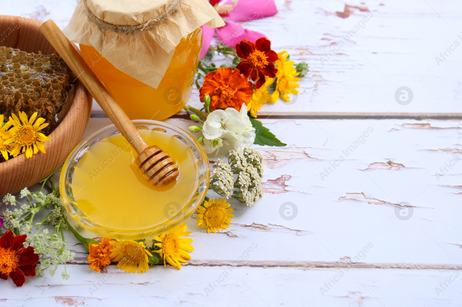 Photo of Delicious honey, combs and different flowers on white wooden table. Space for text