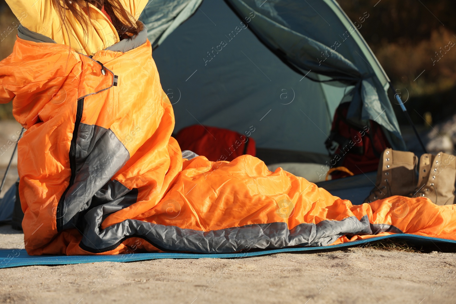 Photo of Woman waking up in sleeping bag near tent outdoors