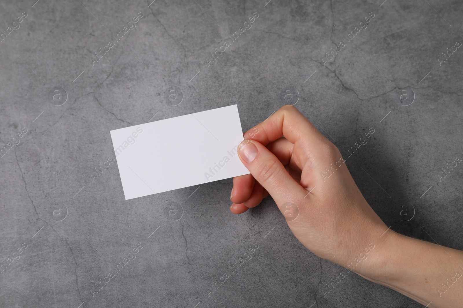 Photo of Woman holding blank card at grey table, top view. Mockup for design