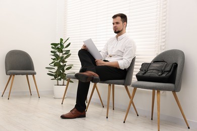 Man with sheet of paper waiting for job interview indoors