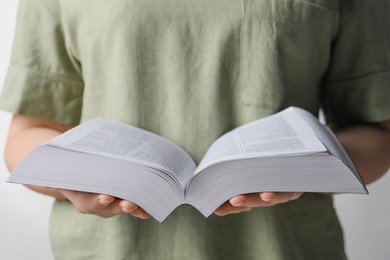Woman with holy Bible against light grey background, closeup