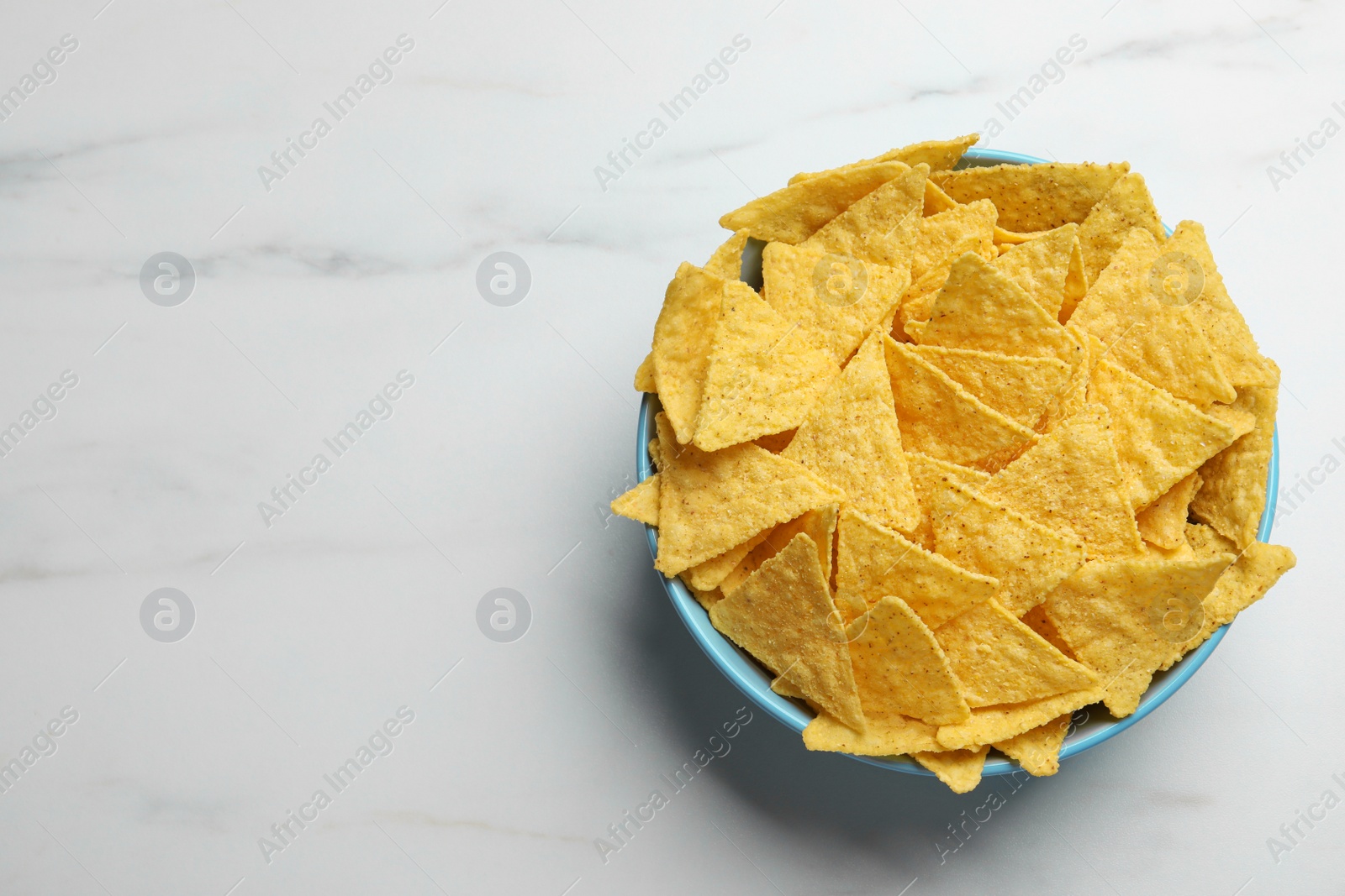 Photo of Tortilla chips (nachos) in bowl on white table, top view. Space for text