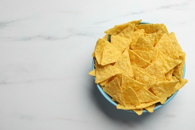 Tortilla chips (nachos) in bowl on white table, top view. Space for text