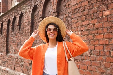 Photo of Young woman with stylish bag near red brick wall outdoors