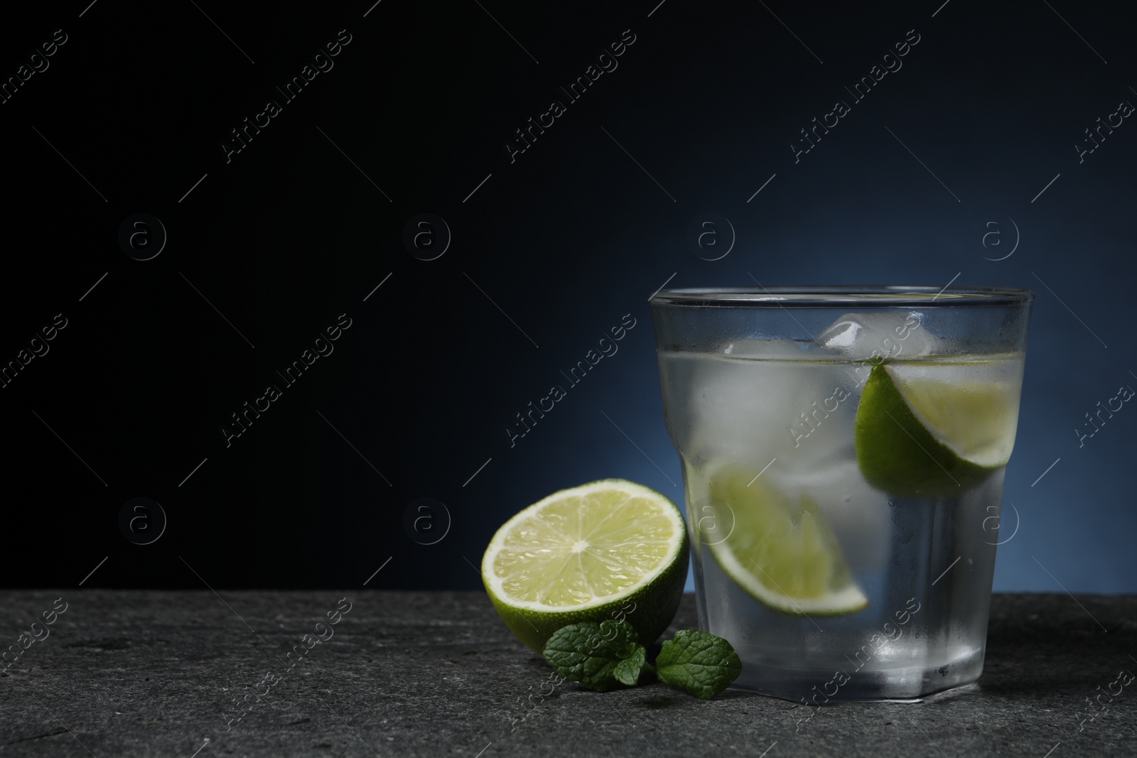 Photo of Glass of vodka with lime slices, mint and ice on grey table. Space for text