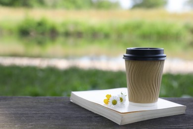 Paper coffee cup, flowers and book on wooden table outdoors, space for text