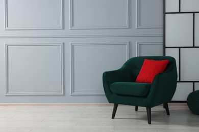 Photo of Comfortable armchair with red pillow near light grey wall indoors. Space for text