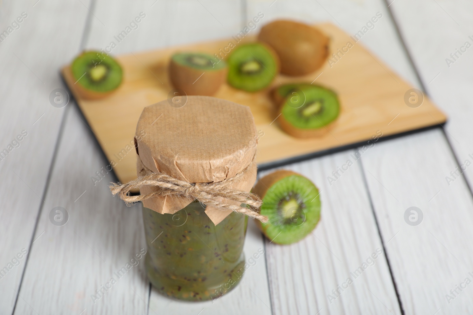 Photo of Jar of delicious kiwi jam and fresh fruits on white wooden table